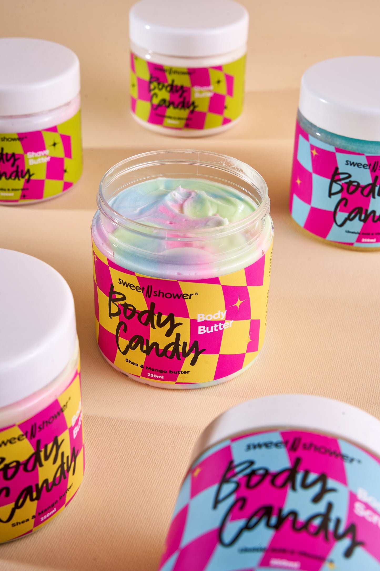 Jars of 'Body Candy' body butter with colorful packaging with colored body scrub on a beige background